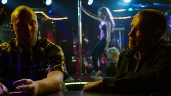 Movie still from “Sabotage” (2014), directed by David Ayer – Two men sitting at a table in front of a pole dancer; Medium shot, Over the shoulder angle