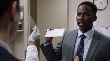Movie still from “Sabotage” (2014), directed by David Ayer – A man in a suit and tie holding a piece of paper; Close Up shot, Over the shoulder angle