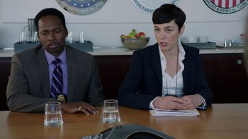 Movie still from “Sabotage” (2014), directed by David Ayer – Two people are sitting at a table in front of a phone; Medium shot, Over the shoulder angle