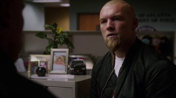 Movie still from “Sabotage” (2014), directed by David Ayer – A bald man with a beard is sitting in front of a desk; Close Up shot, Over the shoulder angle