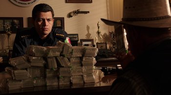 Movie still from “Sabotage” (2014), directed by David Ayer – A man sitting in front of a stack of money; Medium shot, Over the shoulder angle