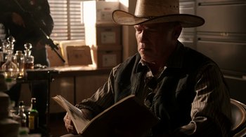 Movie still from “Sabotage” (2014), directed by David Ayer – An older man wearing a cowboy hat reading a book; Medium shot, Over the shoulder angle