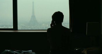 Movie still from “Saint Laurent” (2014), directed by Bertrand Bonello – A person on a cell phone in front of the eiffel tower; Medium shot, Over the shoulder angle