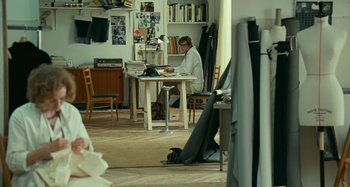 Movie still from “Saint Laurent” (2014), directed by Bertrand Bonello – A person sitting at a table in a room; Wide shot, Over the shoulder angle