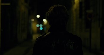 Movie still from “Saint Laurent” (2014), directed by Bertrand Bonello – A person is standing in the dark near some lights; Close Up shot, Over the shoulder angle