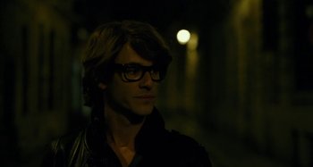 Movie still from “Saint Laurent” (2014), directed by Bertrand Bonello – A young man wearing glasses and a black jacket; Close Up shot, Over the shoulder angle
