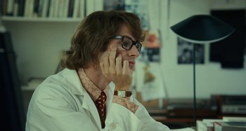 Movie still from “Saint Laurent” (2014), directed by Bertrand Bonello – A man in a white lab coat talking on a cell phone; Close Up shot, Over the shoulder angle