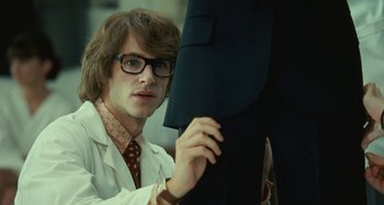 Movie still from “Saint Laurent” (2014), directed by Bertrand Bonello – A man in a white lab coat holding up a suit jacket; Medium shot, Over the shoulder angle