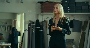 Movie still from “Saint Laurent” (2014), directed by Bertrand Bonello – A woman smoking a cigarette while wearing a black suit; Medium shot, Over the shoulder angle