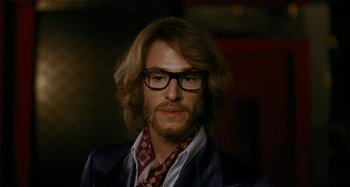Movie still from “Saint Laurent” (2014), directed by Bertrand Bonello – A person wearing glasses and a jacket; Close Up shot, Over the shoulder angle