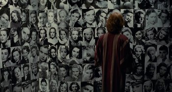 Movie still from “Saint Laurent” (2014), directed by Bertrand Bonello – A woman standing in front of a wall with many different women's faces on it; Medium shot, Over the shoulder angle