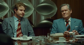 Movie still from “Saint Laurent” (2014), directed by Bertrand Bonello – Two men sitting at a table in front of each other; Medium shot, Over the shoulder angle