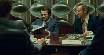 Movie still from “Saint Laurent” (2014), directed by Bertrand Bonello – A man sitting at a table with two other men; Medium shot, Over the shoulder angle