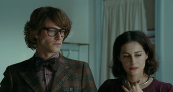 Movie still from “Saint Laurent” (2014), directed by Bertrand Bonello – A man and a woman standing next to each other in a room; Close Up shot, Over the shoulder angle
