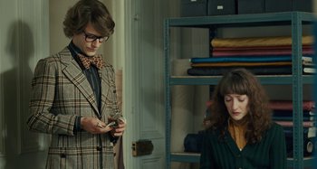 Movie still from “Saint Laurent” (2014), directed by Bertrand Bonello – A man and a woman looking at a cell phone in a room; Medium shot, Over the shoulder angle