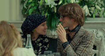 Movie still from “Saint Laurent” (2014), directed by Bertrand Bonello – A man and a woman sitting in front of a wine glass; Medium shot, Over the shoulder angle