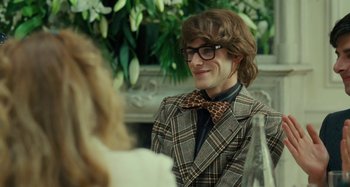 Movie still from “Saint Laurent” (2014), directed by Bertrand Bonello – A man in a suit and bow tie smiling; Close Up shot, Over the shoulder angle