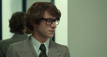 Movie still from “Saint Laurent” (2014), directed by Bertrand Bonello – A man with long hair wearing a suit and glasses; Close Up shot, Over the shoulder angle