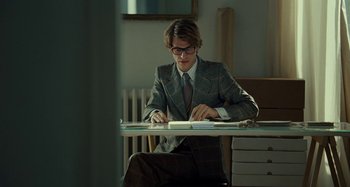 Movie still from “Saint Laurent” (2014), directed by Bertrand Bonello – A man in a suit and tie sitting at a table; Medium shot, Low angle