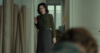 Movie still from “Saint Laurent” (2014), directed by Bertrand Bonello – A woman standing in a room wearing a green shirt; Medium shot, Over the shoulder angle