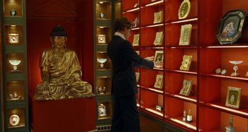 Movie still from “Saint Laurent” (2014), directed by Bertrand Bonello – A man in a suit and tie looking at pictures on a shelf; Medium shot, High angle