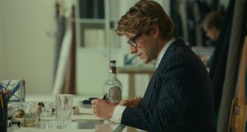 Movie still from “Saint Laurent” (2014), directed by Bertrand Bonello – A man sitting at a table writing on a piece of paper; Medium shot, Over the shoulder angle