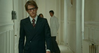 Movie still from “Saint Laurent” (2014), directed by Bertrand Bonello – A man in a suit and tie standing in a hallway; Medium shot, Over the shoulder angle