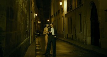 Movie still from “Saint Laurent” (2014), directed by Bertrand Bonello – A man and a woman standing next to each other on a street; Wide shot, Low angle