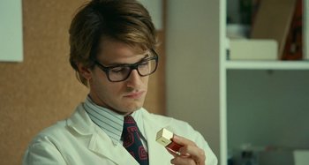 Movie still from “Saint Laurent” (2014), directed by Bertrand Bonello – A man in a white lab coat holding a piece of paper; Close Up shot, Low angle