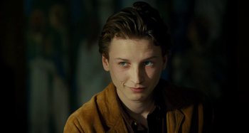 Movie still from “Saint Laurent” (2014), directed by Bertrand Bonello – A young man in a brown jacket looking at the camera; Close Up shot, Over the shoulder angle