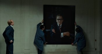 Movie still from “Saint Laurent” (2014), directed by Bertrand Bonello – Two men are hanging a large portrait of a man; Medium shot, Over the shoulder angle