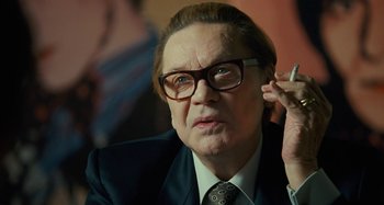 Movie still from “Saint Laurent” (2014), directed by Bertrand Bonello – An older man in a suit and glasses is talking on a cell phone; Close Up shot, Over the shoulder angle