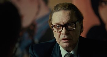 Movie still from “Saint Laurent” (2014), directed by Bertrand Bonello – An older man wearing glasses and a suit; Close Up shot, Over the shoulder angle