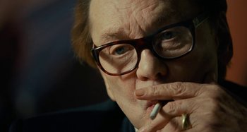 Movie still from “Saint Laurent” (2014), directed by Bertrand Bonello – An older man wearing glasses and smoking a cigarette; Close Up shot, Over the shoulder angle