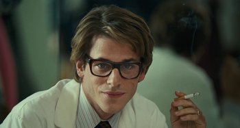 Movie still from “Saint Laurent” (2014), directed by Bertrand Bonello – A young man wearing a white lab coat and glasses; Close Up shot, Over the shoulder angle