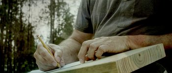 Movie still from “Sandpaper” (2018), directed by Jarett Bellucci – A man writing on a piece of wood with a pair of pencils; Extreme Close Up shot, Low angle