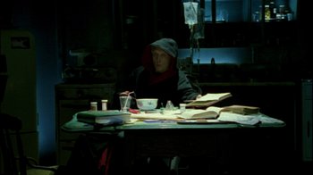 Movie still from “Saw II” (2005), directed by Darren Lynn Bousman – A man sitting at a table with a cup of coffee; Medium shot, High angle