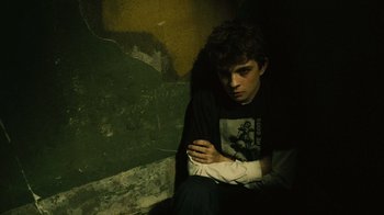 Movie still from “Saw II” (2005), directed by Darren Lynn Bousman – A young man sitting against a wall with his arm in a cast; Medium shot, High angle