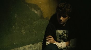 Movie still from “Saw II” (2005), directed by Darren Lynn Bousman – A man sitting on the ground with his arm wrapped around his elbow; Medium shot, High angle