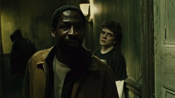 Movie still from “Saw II” (2005), directed by Darren Lynn Bousman – A man standing next to another man in a dark room; Close Up shot, Over the shoulder angle