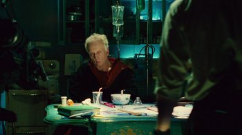 Movie still from “Saw II” (2005), directed by Darren Lynn Bousman – An older man sitting at a table in a room; Medium shot, Over the shoulder angle