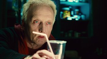 Movie still from “Saw II” (2005), directed by Darren Lynn Bousman – An older man drinking from a cup with a straw; Close Up shot, High angle