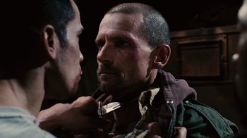 Movie still from “Saw II” (2005), directed by Darren Lynn Bousman – A man with a knife in his mouth and another man with a knife in his other hand; Close Up shot, Over the shoulder angle