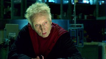 Movie still from “Saw II” (2005), directed by Darren Lynn Bousman – An older man with blonde spiky hair wearing a red and black shirt; Close Up shot, Over the shoulder angle