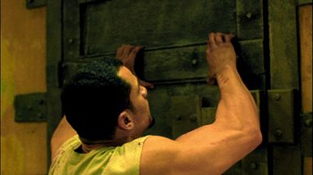 Movie still from “Saw II” (2005), directed by Darren Lynn Bousman – A man in a yellow shirt is holding on to a wall; Close Up shot, Low angle