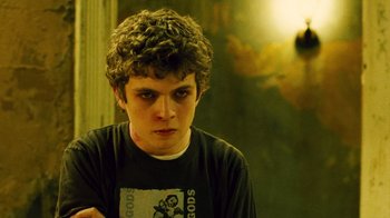 Movie still from “Saw II” (2005), directed by Darren Lynn Bousman – A young man with curly brown hair wearing a t - shirt; Close Up shot, Over the shoulder angle