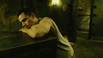 Movie still from “Saw II” (2005), directed by Darren Lynn Bousman – A man laying on the ground with his head on a table; Medium shot, High angle