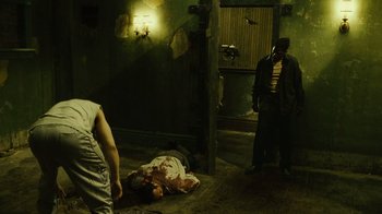 Movie still from “Saw II” (2005), directed by Darren Lynn Bousman – Two men standing next to a dead body in a dark room; Wide shot, High angle