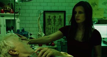 Movie still from “Saw III” (2006), directed by Darren Lynn Bousman – A woman is giving a man an injection in her hand; Medium shot, Low angle