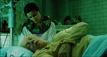 Movie still from “Saw III” (2006), directed by Darren Lynn Bousman – A woman standing next to an old man in a hospital bed; Medium shot, High angle
